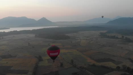 Red-and-blue-hot-air-balloon-flight-above-flat-field-and-water-landscapes-at-sunny-morning---Aerial-drone-view-4k