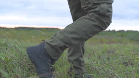 Low-angle-shot-of-person-walking-on-green-grass-field-outdoors-with-military-protection-outfit