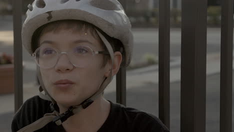 Cute-kid-sitting-outside-at-golden-hour-with-a-bike-helmet-on-and-glasses-smiles-a-big-smile