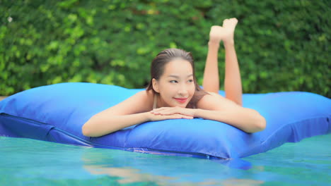 Close-up-of-a-pretty-young-woman-floating-on-a-huge-blue-float-in-the-middle-of-a-luxury-resort-pool