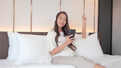 Attractive-Young-Woman-Listening-to-Music-on-the-Bed-with-Smartphone