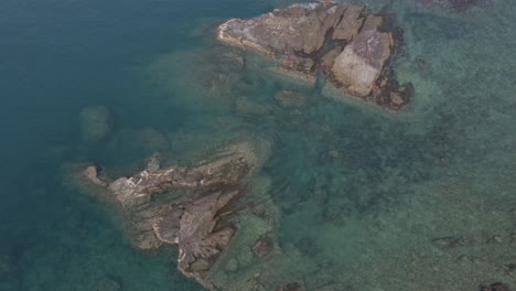 Aerial-birds-eye-view-dolly-shot-of-Granite-rocks-come-out-of-the-clear-blue-sea-with-coral-reef-around