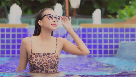 A-glamorous-young-woman-in-leopard-print-swimwear-turns-her-head-and-adjusts-her-sunglasses-while-enjoying-the-resort-pool-amenities