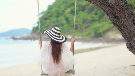 Back-of-young-woman-on-a-tree-swing-by-exotic-tropical-white-sand-beach-and-sea,-Luxury-vacation-concept,-slow-motion-full-frame