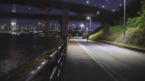 Bicycle-rider-passing-under-Cheongdam-Bridge-near-Han-River-In-Seoul,-South-Korea-At-Night---static-wide-angle-shot