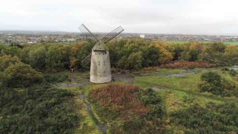 Traditional-wooden-stone-flour-mill-windmill-preserved-in-Autumn-woodland-aerial-view-countryside-pull-away-orbit-right