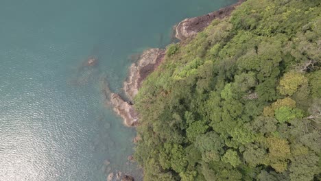 Aerial,-birds-eye-view-of-tropical-rocky-granite-ocean-coastline-with-lush-tropical-forest-vegetation-on-a-Island