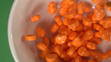 Close-up-of-orange-skulls-and-bones-shaped-candy-falling-on-a-plate,-on-a-chroma-background