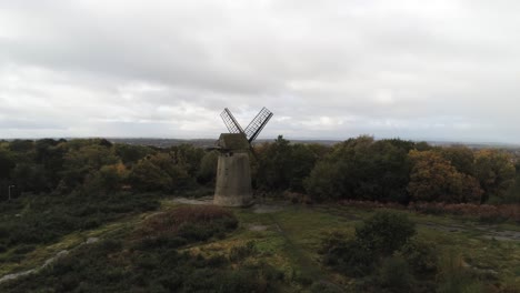 Traditional-wooden-stone-flour-mill-windmill-preserved-in-Autumn-woodland-aerial-view-countryside-right-slow-dolly