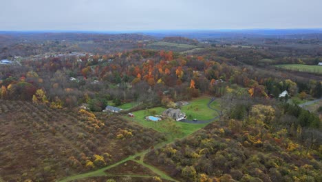Flying-over-an-autumnal-valley-with-deciduous-trees-and-a-residential-neighborhood