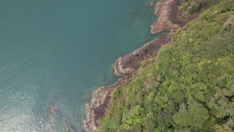Aerial,-birds-eye-view-dolly-spin-rotating-shot-of-tropical-rocky-granite-ocean-coastline-with-lush-tropical-forest-vegetation-on-a-Island-in-Thailand