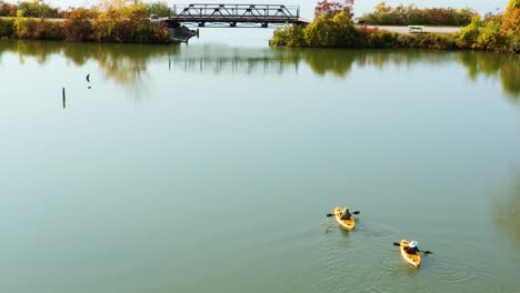 An-aerial-view-of-two-people-slowly-kayaking-away-from-the-camera-towards-a-pedestrian-bridge