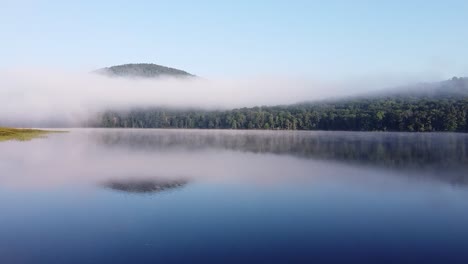 skimming-over-water-on-calm,-peaceful-forest-lake-on-early,-misty-morning