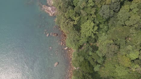 Aerial,-birds-eye-view,-dolly-spin-left-rotation-shot-of-tropical-rocky-granite-ocean-coastline-with-lush-tropical-forest-vegetation-on-a-Island
