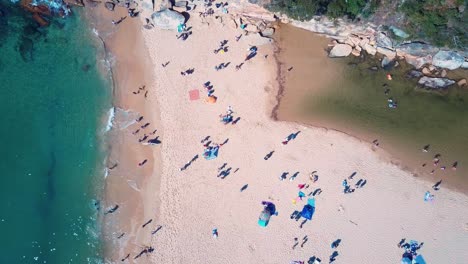 Busy-beach-in-bay-of-Wattamolla-were-creek-meets-sea-in-Australia,-aerial