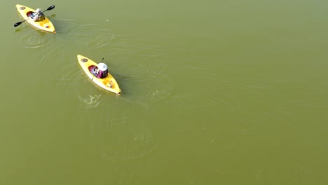 A-close-up-aerial-view-of-two-people-slowly-kayaking-from-the-bottom-middle-to-the-top-left-of-the-screen-on-a-calm,-sunny-day
