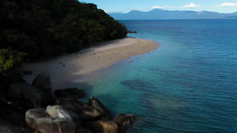 Revealing-drone-shot-of-woman-walking-in-the-water-at-Fitzroy-Island-beach-in-Australia