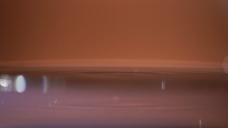 Wassertropfen-Auf-Der-Wasseroberfläche-Auf-Glänzend-Orangefarbenem-Hintergrund-Hautnah