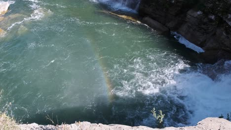 Mist-from-waterfall-creates-vivid,-colourful-rainbow-over-green-river
