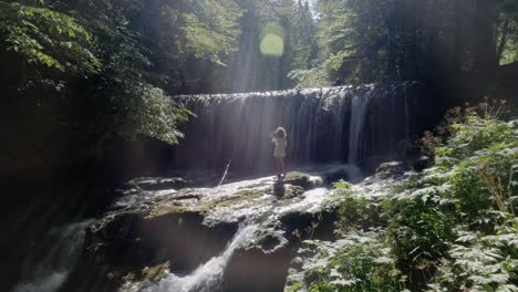 Drone-shot-of-a-young-woman-in-front-of-a-beautiful-waterfall-in-spring