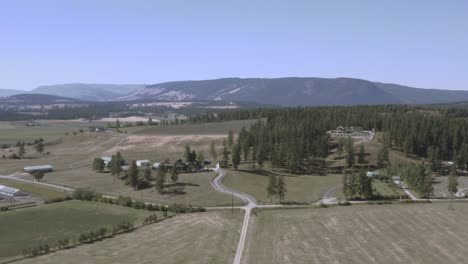 aerial-panout-fly-over-cattle-farms-rolling-hills-within-a-mountain-valley-township-with-luxury-estates-around-ranches-curvy-roads-on-a-hot-clear-summer-day-with-moder-barns-tall-lush-pine-trees-2-2