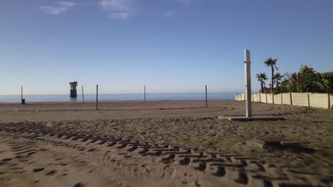 Moving-forward-at-the-empty-beach-of-Marbella,-Spain,-with-an-abandoned-overhead-cable-tower-in-the-sea