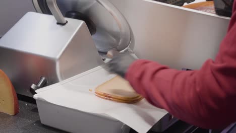 A-uniformed,-gloved-deli-worker-slices-cheese-using-an-industrial-cutter