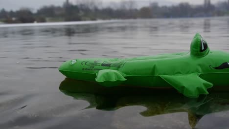 Ein-Grünes-Aufblasbares-Krokodil-Schwimmt-Von-Links-Nach-Rechts-Auf-Einem-See