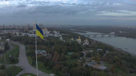 Aerial-View-Of-Ukrainian-Flag-And-Kyiv-Pechersk-Lavra,-A-Historic-Monastery-In-Kyiv,-Ukraine---drone-shot