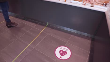 Social-distancing-sticker-signs-on-a-deli-floor-indicate-where-a-customer-should-stand