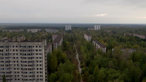 Aerial-View-Of-Empty-Street-Surrounded-By-Deserted-Buildings-And-Trees-In-Pripyat,-Ukraine-During-Autumn---Chernobyl-Disaster---drone-shot