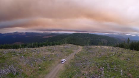Camper-Van-travels-alone-down-a-dirt-road-in-the-mountains-with-smoky-skies,-Aerial-high-frame-rate-59