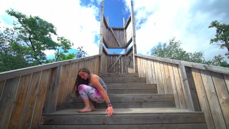 Young-woman-doing-yoga-exercise-bridge-pose-outdoors-wooden-stairs-garden,-day