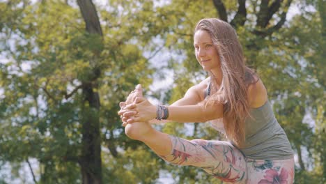 Caucasian-woman-holds-leg-yoga-pose-in-nature,-slow-motion-medium-shot
