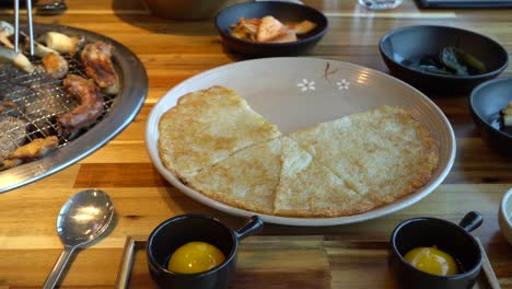 Grilling-Korean-Chicken-Barbecue-With-Egg-Yolk,-Side-Dish,-And-Korean-Potato-Pancake-On-Table-In-Restaurant-In-Chuncheon-City,-South-Korea