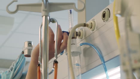 Nurse-hand-adjusts-medical-flowmeter-and-humidifier-in-hospital,-close-up
