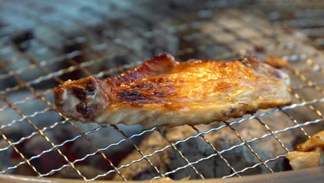Turning-marinated-chicken-wing-with-tong-on-Korean-Barbecue,-close-up