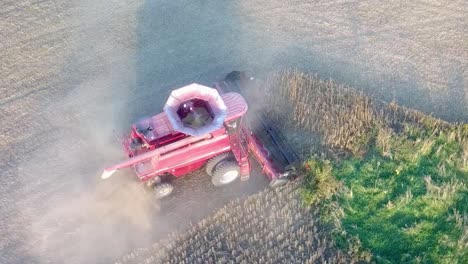 Aerial-drone-pan-view-of-red-combine-picking-soybeans-around-a-wet-patch-in-a-dusty-field-about-an-hour-before-sundown