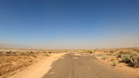 Eine-Trostlose-Mojave-Wüstenstraße-Hinunterfahren,-Die-Von-Wind-Und-Stürmen-Mit-Sand-Bedeckt-Ist---Standpunkt