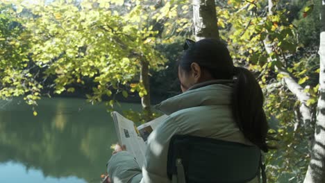 Girl-reading-magazine-in-nature-and-enjoy-lake-view-close-up