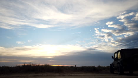 Gleitbewegungszeitraffer-Mit-Der-Silhouette-Eines-Jeeps-Im-Vordergrund,-Während-Die-Sonnenuntergangswolken-über-Den-Himmel-über-Der-Mojave-Wüste-Rollen