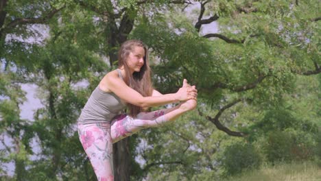 Side-view-of-young-woman,-performing-standing-head-to-knee-yoga-pose-outdoors