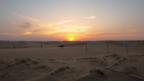 Ascending-over-Abu-Dhabi-desert-sand-dune-to-reveal-marvelous-orange-and-pink-sun-setting-over-horizon