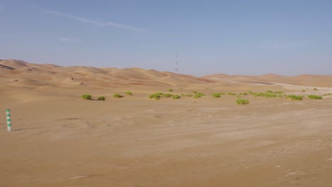 Fahren-Sie-Durch-Die-Erstaunlichen-Leeren-Straßen-Der-Wüste-Von-Abu-Dhabi-Mit-Kleinen-Grünen-Sträuchern-Am-Fuße-Der-Sanddünen