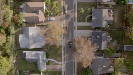 Overhead-view-of-suburban-neighborhood-in-Autumn-as-a-car-drives-down-the-street-and-pulls-into-a-driveway