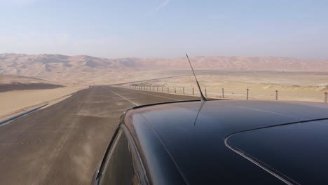 Looking-Behind-Over-Rooftop-of-Black-Car-driving-through-Spectacular-Empty-Abu-Dhabi-Desert-Road