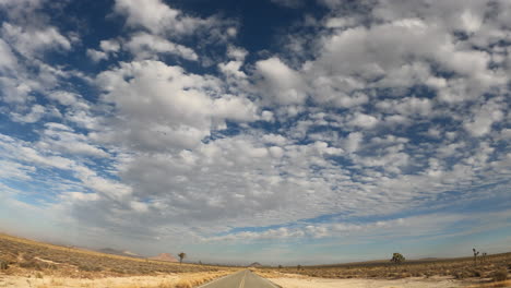 Driving-along-a-road-straight-through-the-Mojave-Desert-toward-the-distant-mountains---point-of-view