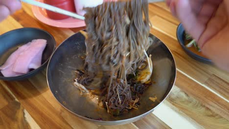 Hands-mixing-buckwheat-noodles-in-bowl-with-steel-chopsticks,-Korean-Cuisine