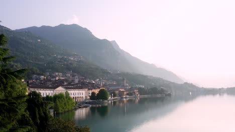 Drone-view-of-Lake-Iseo-at-sunrise,-on-the-left-the-city-of-Lovere-which-runs-along-the-lake,Bergamo-Italy