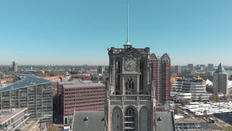 Aerial-drone-footage-rising-along-the-face-of-a-church-tower,-revealing-the-city-of-Rotterdam,-Netherlands